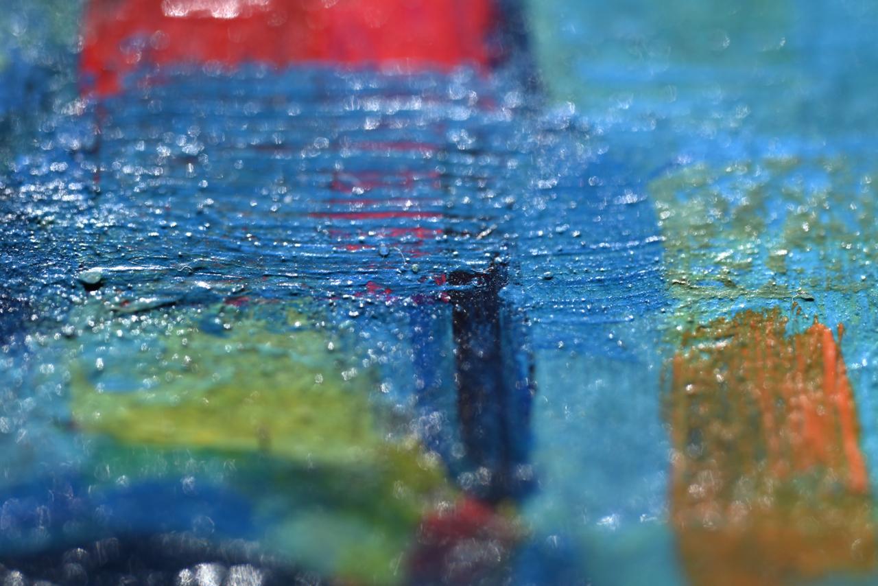 Close-up of an abstract painting with thick blue impasto brushstrokes and accents of red, green and ochre